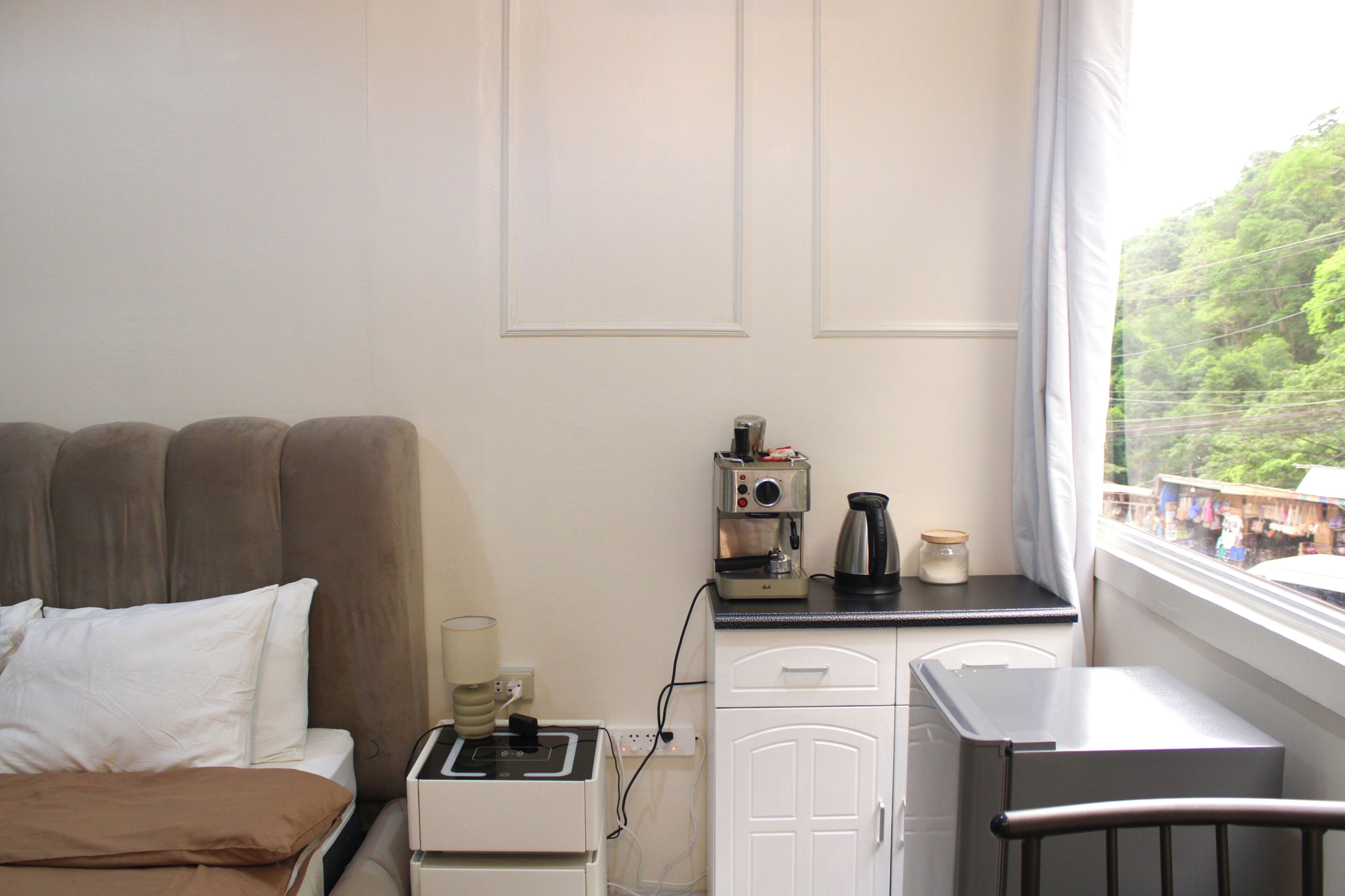 A small, compact room with a bed, a coffee machine, a kettle, and a window with a view of a green landscape.