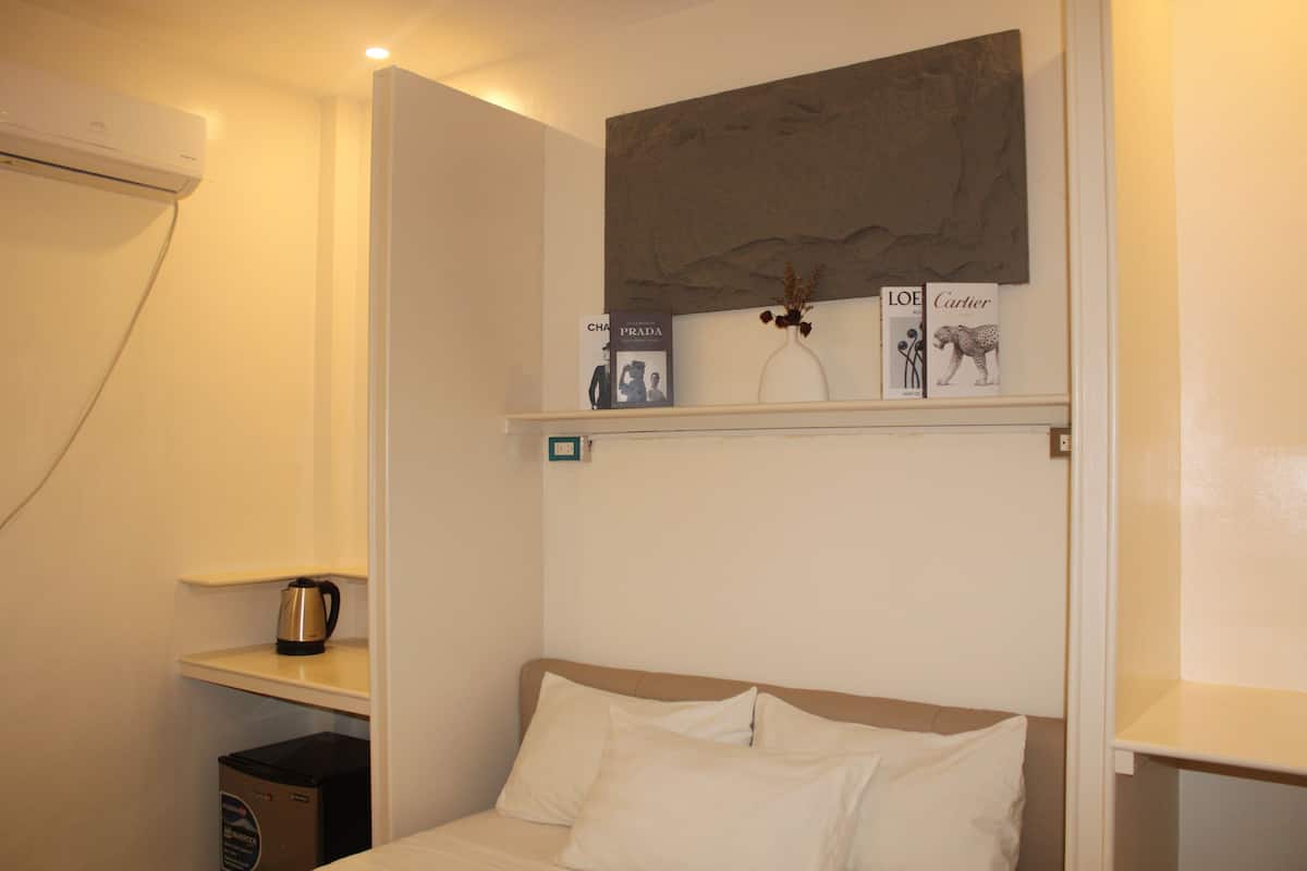 A hotel room with a bed, a shelf with books and a vase, and a coffee maker on a small table.