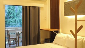 A hotel room with a bed, a small table, a chair, and a view of greenery through the window. - MAYAD El Nido Inn (El Nido)