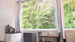 A room with a window overlooking a forest, a small table with chairs, a kitchenette with a refrigerator, and a bed. - MAYAD El Nido Inn (El Nido)