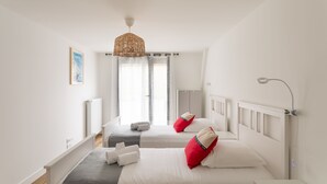 Ein Hotelzimmer mit zwei Betten, einer Pendelleuchte, einem Heizkörper und einem fenster mit Vorhängen.