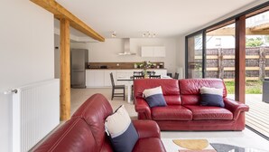 Ein modernes Wohnzimmer mit einem roten Ledersofa, einem Essbereich und einer Küche mit weißen Schränken.