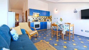 A compact living space with a kitchenette, a dining area, and a sofa with cushions. - Holiday apartment with barbecue (Vinkuran)