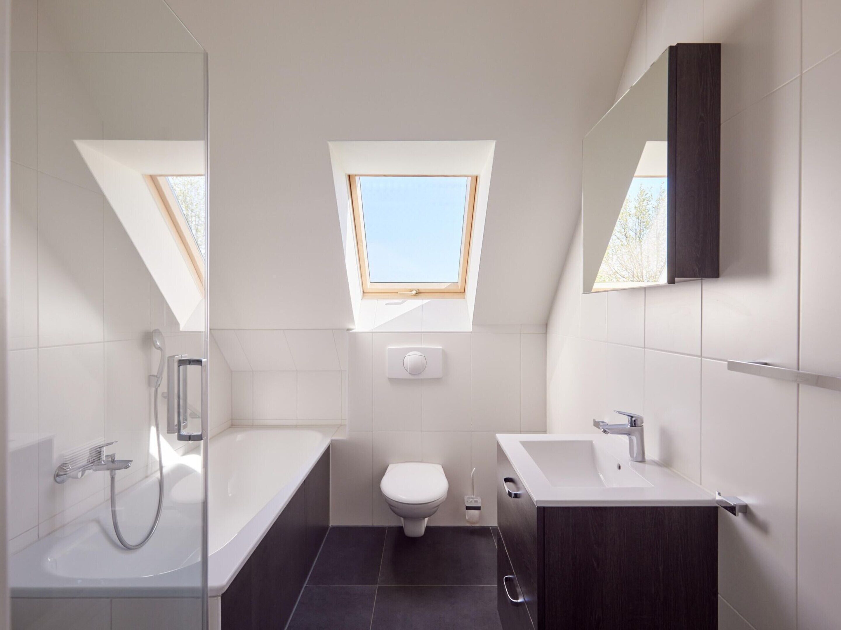 A modern bathroom with a skylight, a bathtub, a toilet, and a sink.