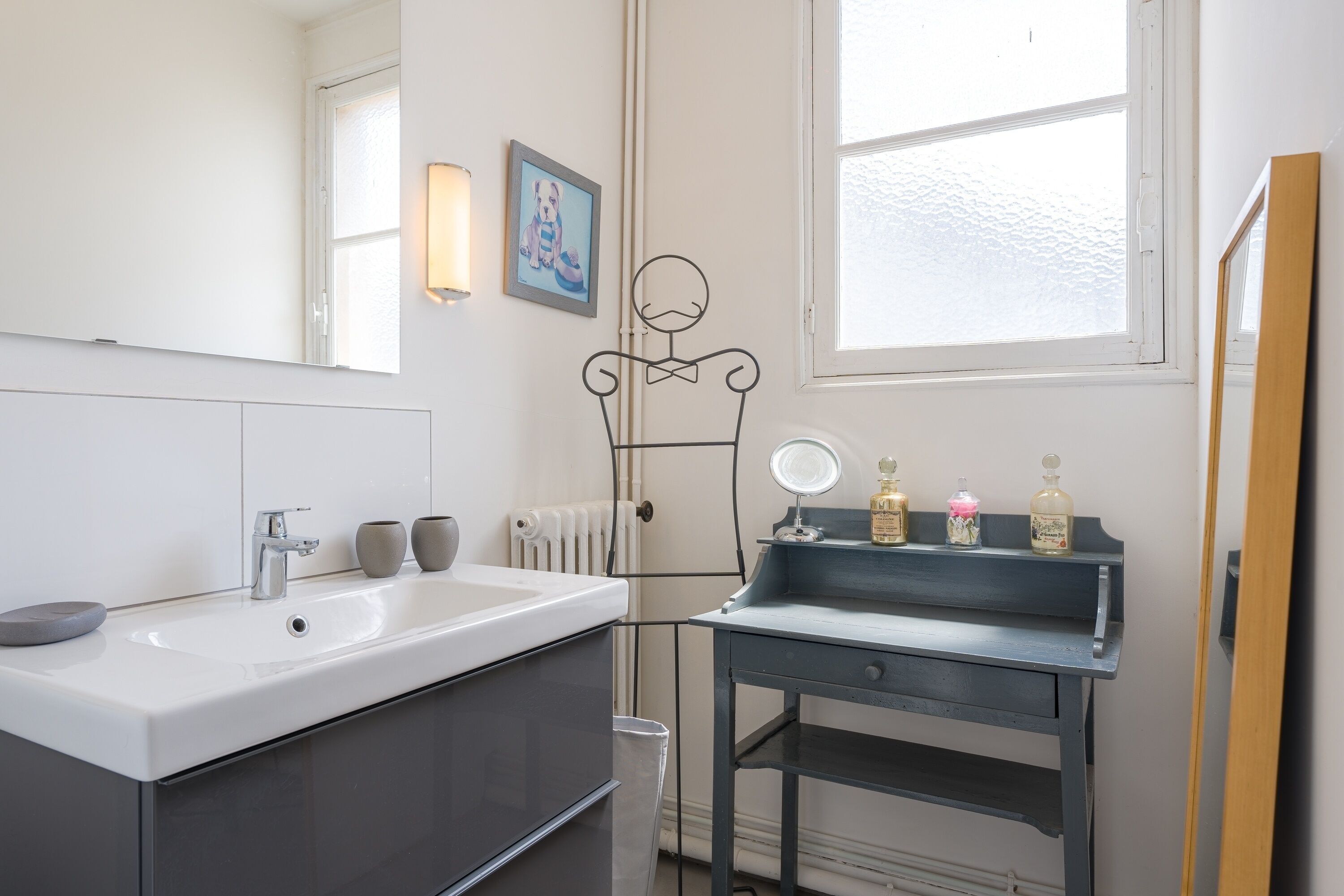 Een moderne badkamer met een witte wastafel, een spiegel en een klein opbergtafeltje met toiletartikelen.