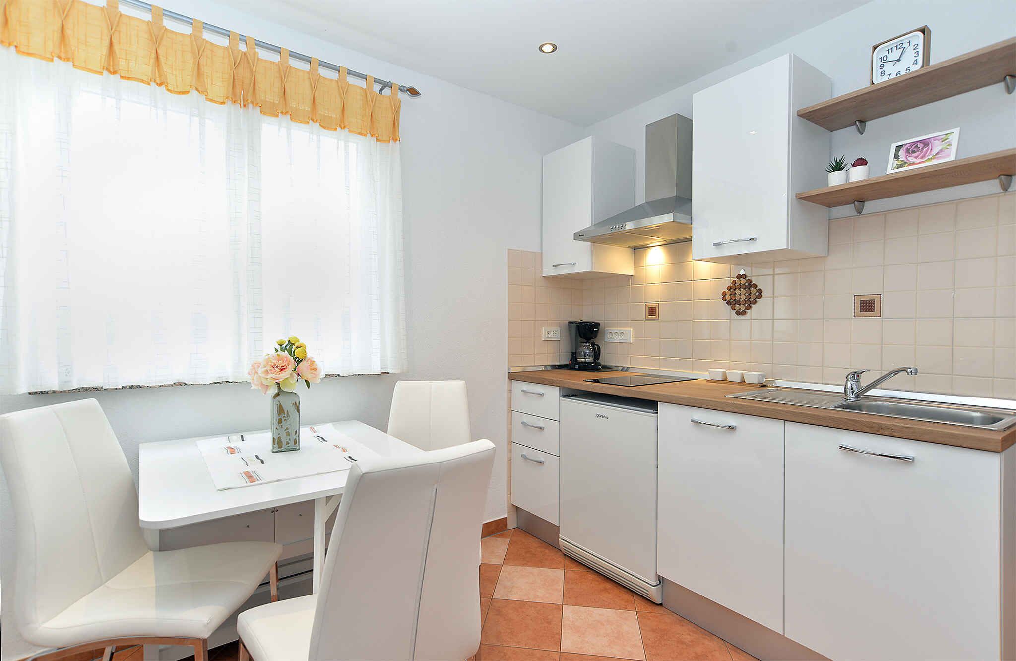 Cocina moderna con armarios blancos, encimera de madera, un lavabo y un comedor con mesa y sillas blancas.