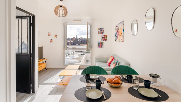 A dining area with a table set for two, a view of the cityscape through the window, and a modern interior design.