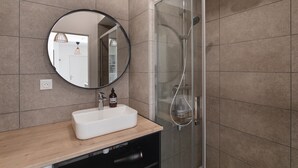 A modern bathroom with a glass shower enclosure, a round mirror, and a wooden vanity.