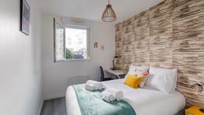 A modern hotel room with a large bed, a desk, and a view of the city through the window.