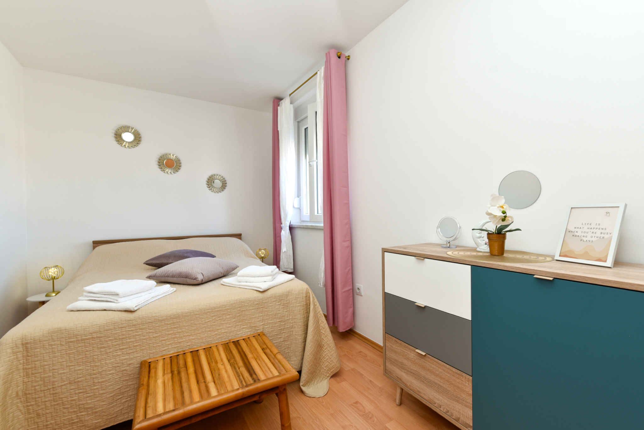 A bedroom with a bed, bedside table, and a desk with a mirror and a potted plant.