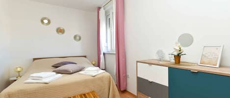 A bedroom with a bed, bedside table, and a desk with a mirror and a potted plant.