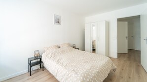 Un dormitori amb llit, una tauleta de nit, un armari i una porta oberta que dona a una altra habitació.