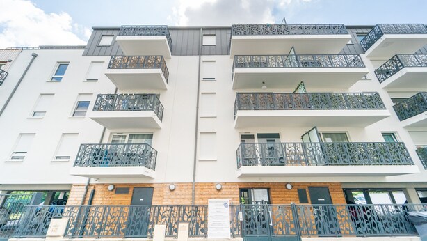 Un edifici residencial de diverses plantes amb balcons, façana de fusta i entrada tancada per una reixa.
