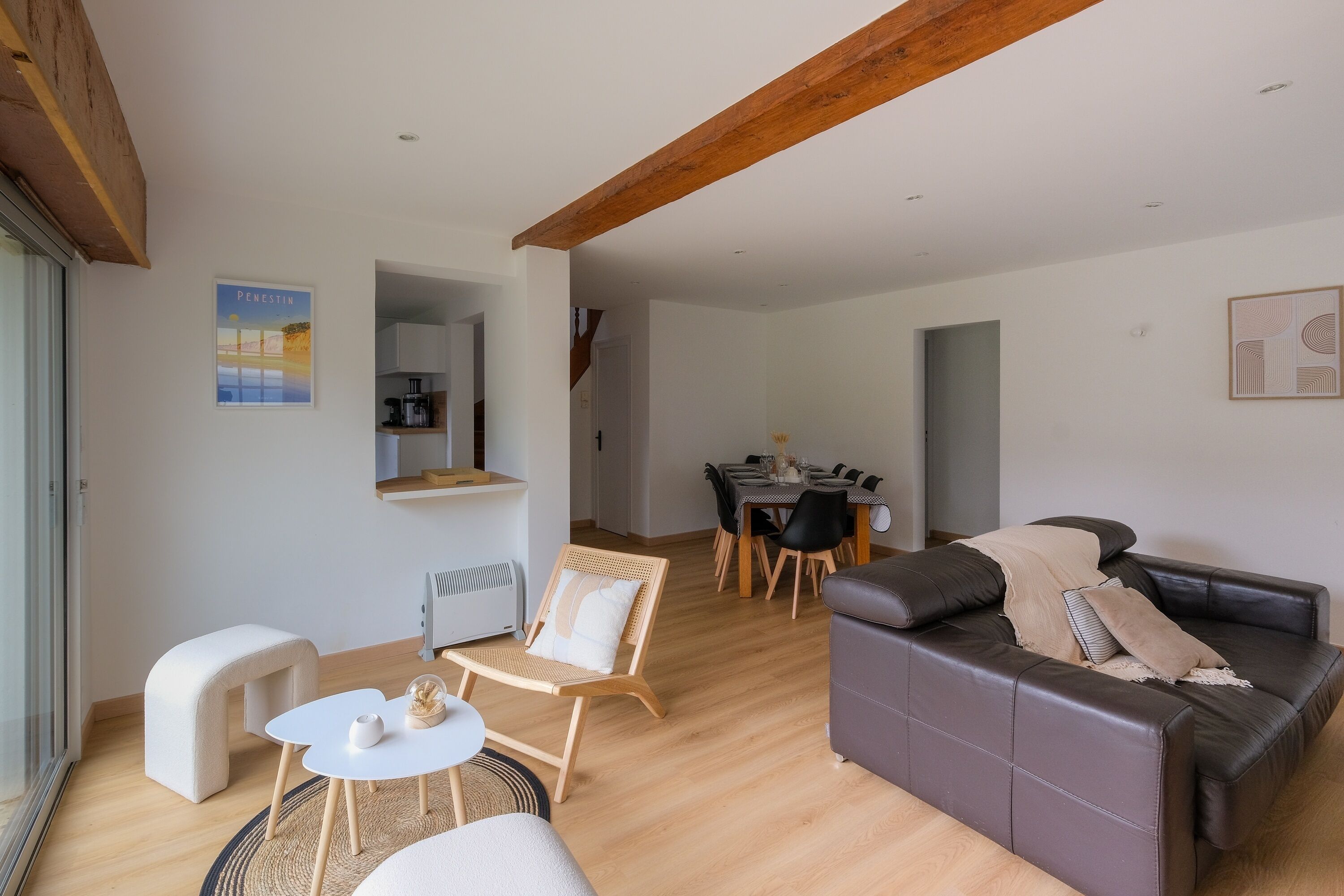A modern living room with a sofa, a small table, and a chair. There is a dining area with a table and chairs in the background.
