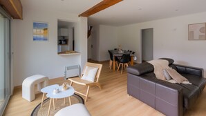 A modern living room with a sofa, a small table, and a chair. There is a dining area with a table and chairs in the background. - Villa Bihen - Maison vue mer, Pénestin (Pénestin)