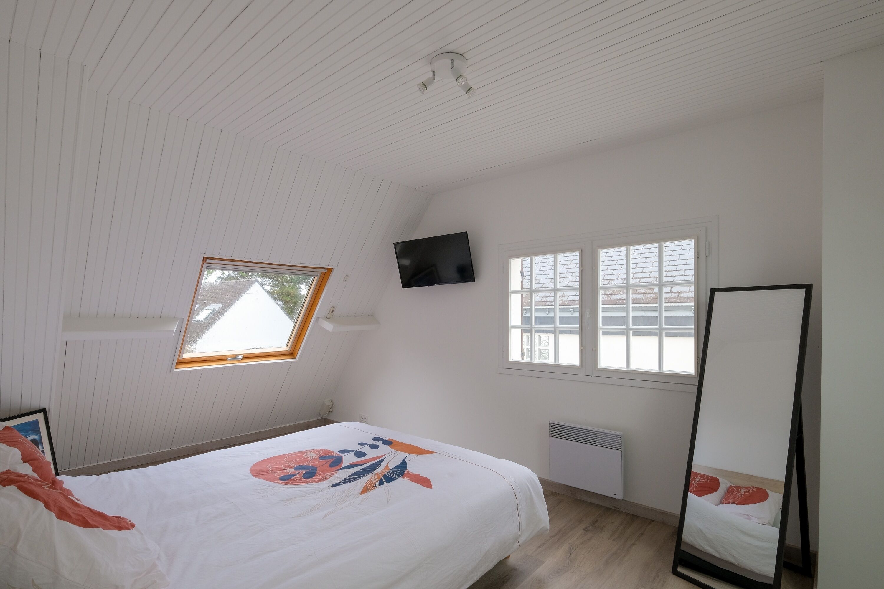 Een slaapkamer met een bed, een aan de muur bevestigde televisie, een raam en een radiator.