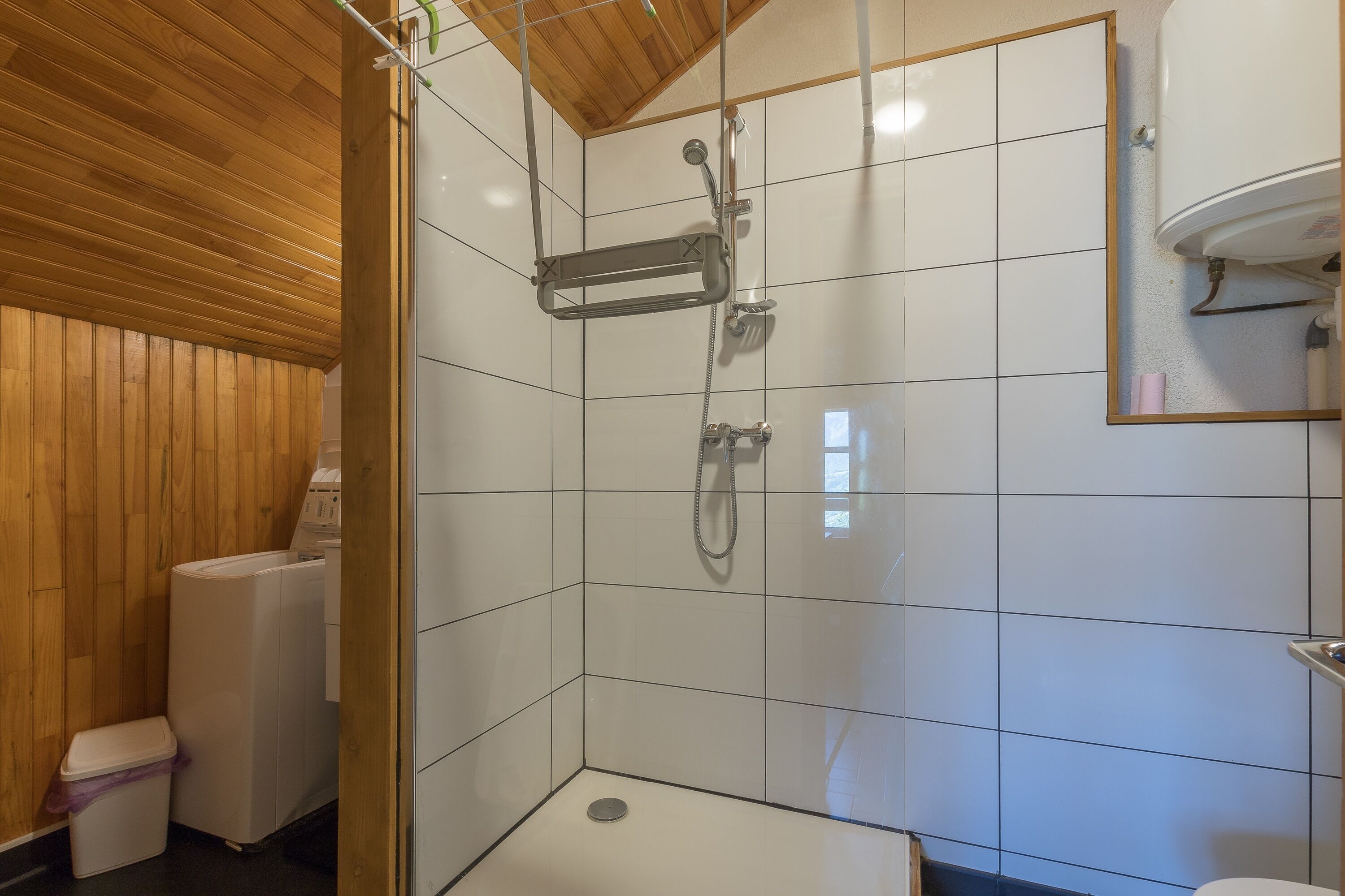 A shower area with a tiled wall, a wooden ceiling, and a toilet.
