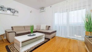 Una sala moderna con un sofá seccional color beige, una mesa de centro blanca y un ventanal con cortinas translúcidas.