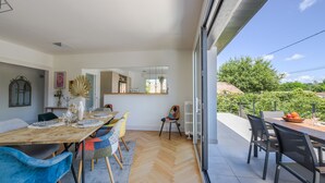 A modern dining area with a wooden table set for four, surrounded by colorful chairs. - Villa Violette - Piscine privée (Gujan-Mestras)