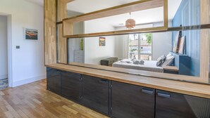 A modern interior with a large mirror reflecting a bedroom, a wooden cabinet, and a hanging light fixture. - Villa Violette - Piscine privée (Gujan-Mestras)