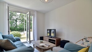 A modern living room with a sofa set, a coffee table, a TV, and a sliding glass door leading to a garden.