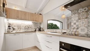 Una cocina moderna con armarios blancos, horno empotrado y ventana con vistas a zonas verdes.