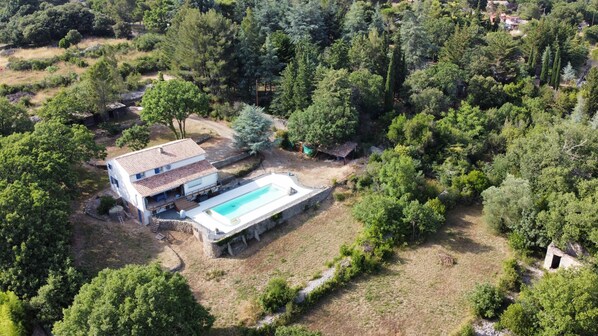 Une maison à deux étages avec une piscine, entourée d’une végétation luxuriante et d’arbres.