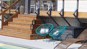 Zona de piscina con escalones de madera que conducen a un área de estar cubierta con sillas y una mesa.