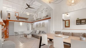 Amplia sala de estar con techo alto, una mesa de comedor con sillas, un sofá y una escalera que conduce a un nivel superior.