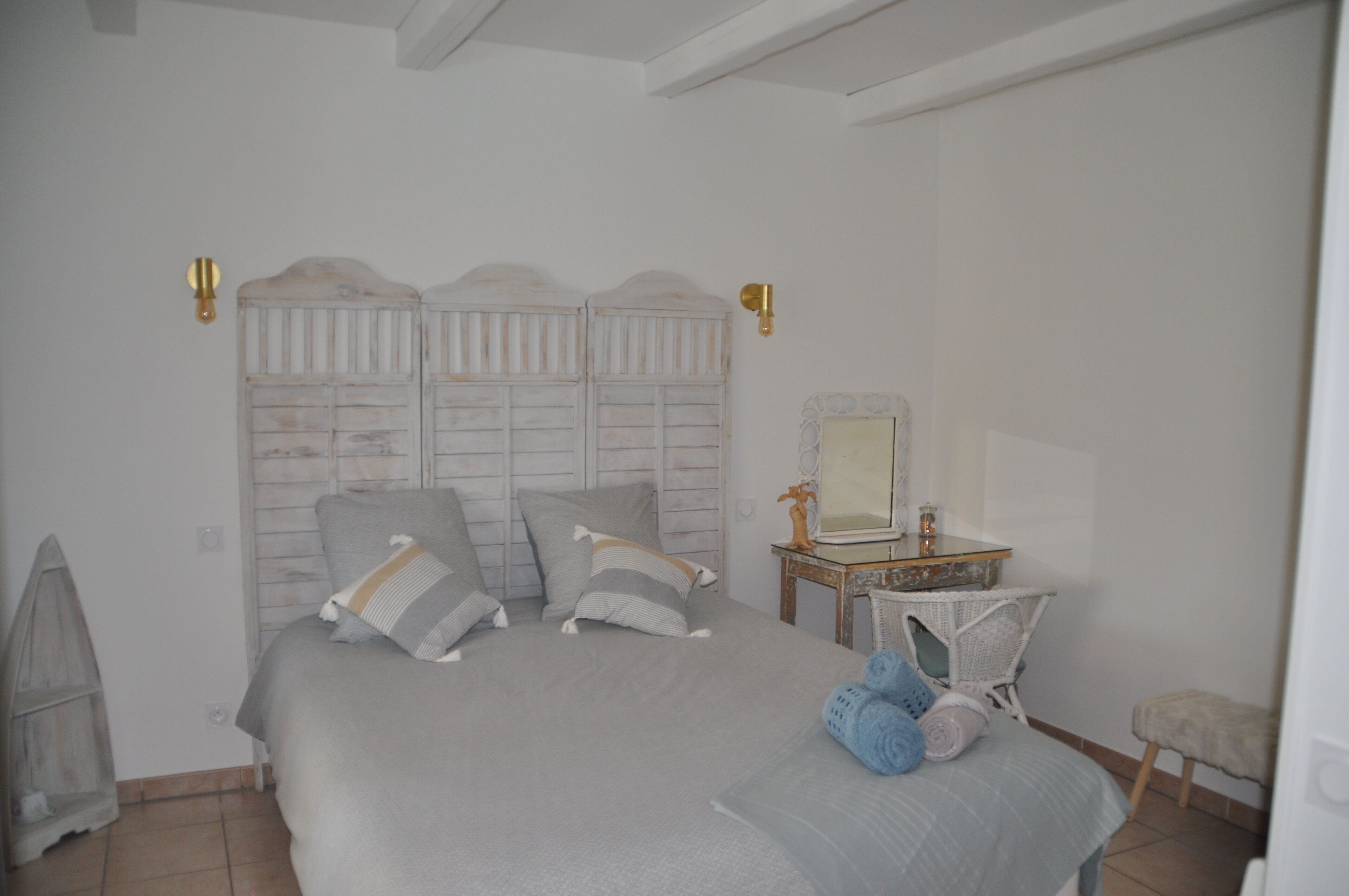 A bedroom with a bed, pillows, a nightstand, a mirror, and a chair.
