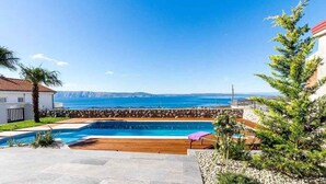 A swimming pool with a view of the sea, surrounded by a stone wall and wooden decking.