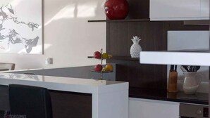 A modern kitchen with a white countertop, a red apple, and a pineapple on a shelf.