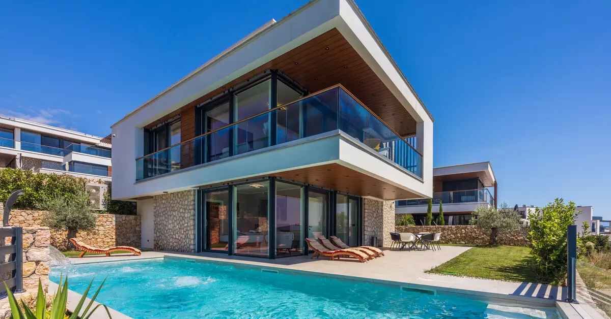 A modern two-story house with a swimming pool, glass railings, and a stone exterior.