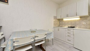 A compact kitchen with white cabinets, a small dining table with chairs, and a tiled backsplash. - Studio with air conditioning (Fažana)