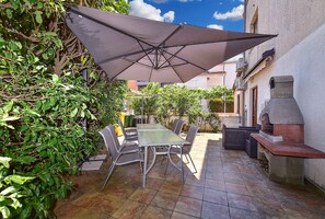 En udendørs terrasse med et bord, stole og en stor parasol samt en stenovn.