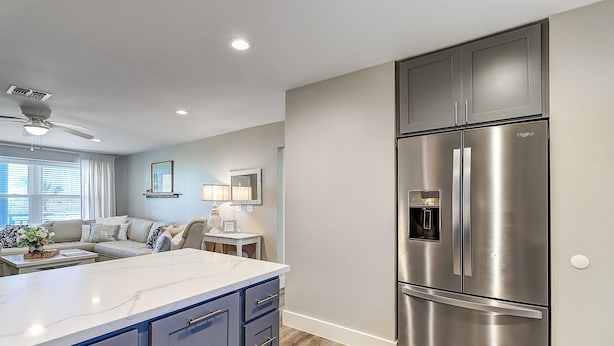 A modern kitchen with a large stainless steel refrigerator, a marble countertop, and a ceiling fan.