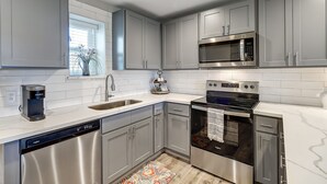 A modern kitchen with stainless steel appliances, grey cabinetry, and a white countertop.