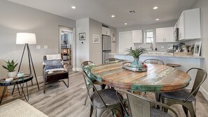 Una cocina moderna con armarios blancos, una mesa de comedor de madera y un pequeño rincón de comedor con lámpara y sillas.