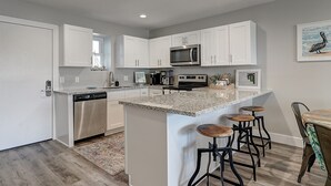 Una cocina moderna con gabinetes blancos, electrodomésticos de acero inoxidable y una isla de granito con taburetes.