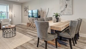 A dining area with a wooden table, grey upholstered chairs, a television, and decorative items.