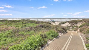 A coastal path leading to the beach with dunes and vegetation.