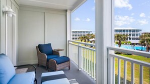A balcony with wicker furniture and a view of a pool and buildings. - Beachfront Luxury with Gulf Views: 3BR/2BA Condo w/ Private Beach Access & Pool (Port Aransas)