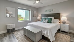 A bedroom with a bed, bedside lamps, a ceiling fan, a window, and a wall-mounted fish decoration. - Beachfront Luxury with Gulf Views: 3BR/2BA Condo w/ Private Beach Access & Pool (Port Aransas)