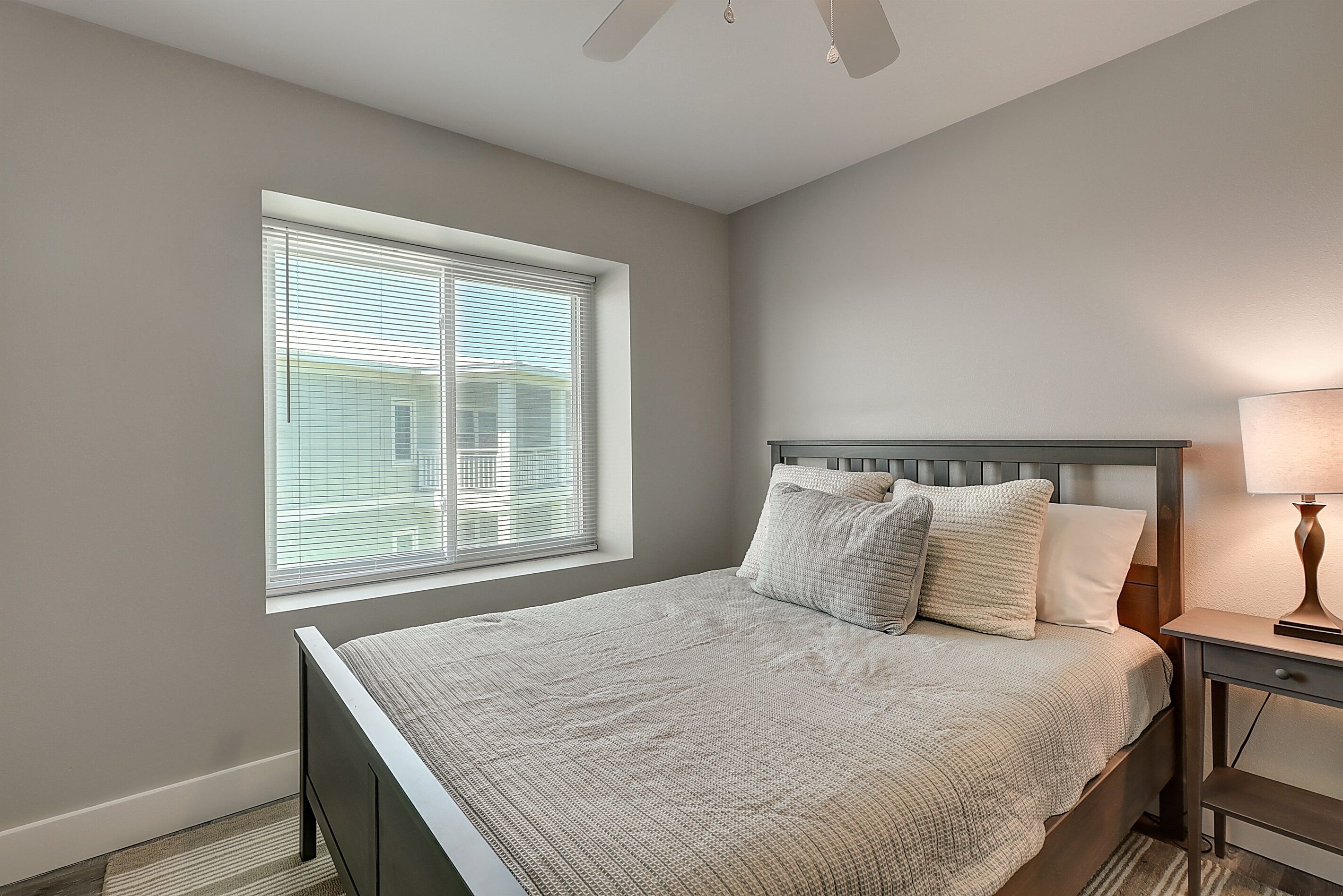 Un dormitorio con cama, mesita de noche, lámpara y ventana con persianas.