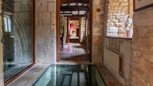 A stone-walled hallway with a glass floor leading to a room with a wooden ceiling and a red rug. - Midsummer Mill - Five Bedroom Apartment, Sleeps 8 (Bourton-on-the-Water)