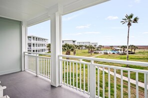 A balcony with a view of a pool and palm trees, a building with balconies, and a clear sky. - Remodeled Beachy 2BR/2BA-Pool View & Walk to Beach (Port Aransas)
