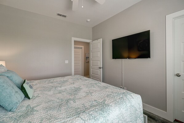 A bedroom with a bed, a television mounted on the wall, and a door leading to another room.