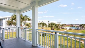Ein überdachter Balkon mit Blick auf einen Pool, Palmen und weitere Gebäude.