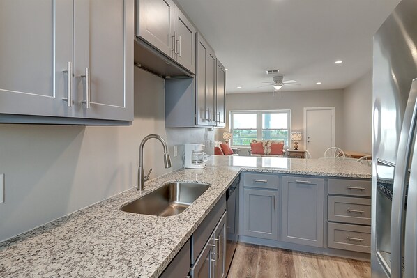 A modern kitchen with granite countertops, stainless steel appliances, and grey cabinetry. - 2BR/2BA Condo w/ Pool View, Private Beach Access, and Walking Distance to Town! (Port Aransas)
