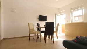 A dining area with a table and four chairs, a flat-screen TV on the wall, and a window with a view of the outside. - Holiday apartment with garden for shared use and children's playground (Ližnjan)